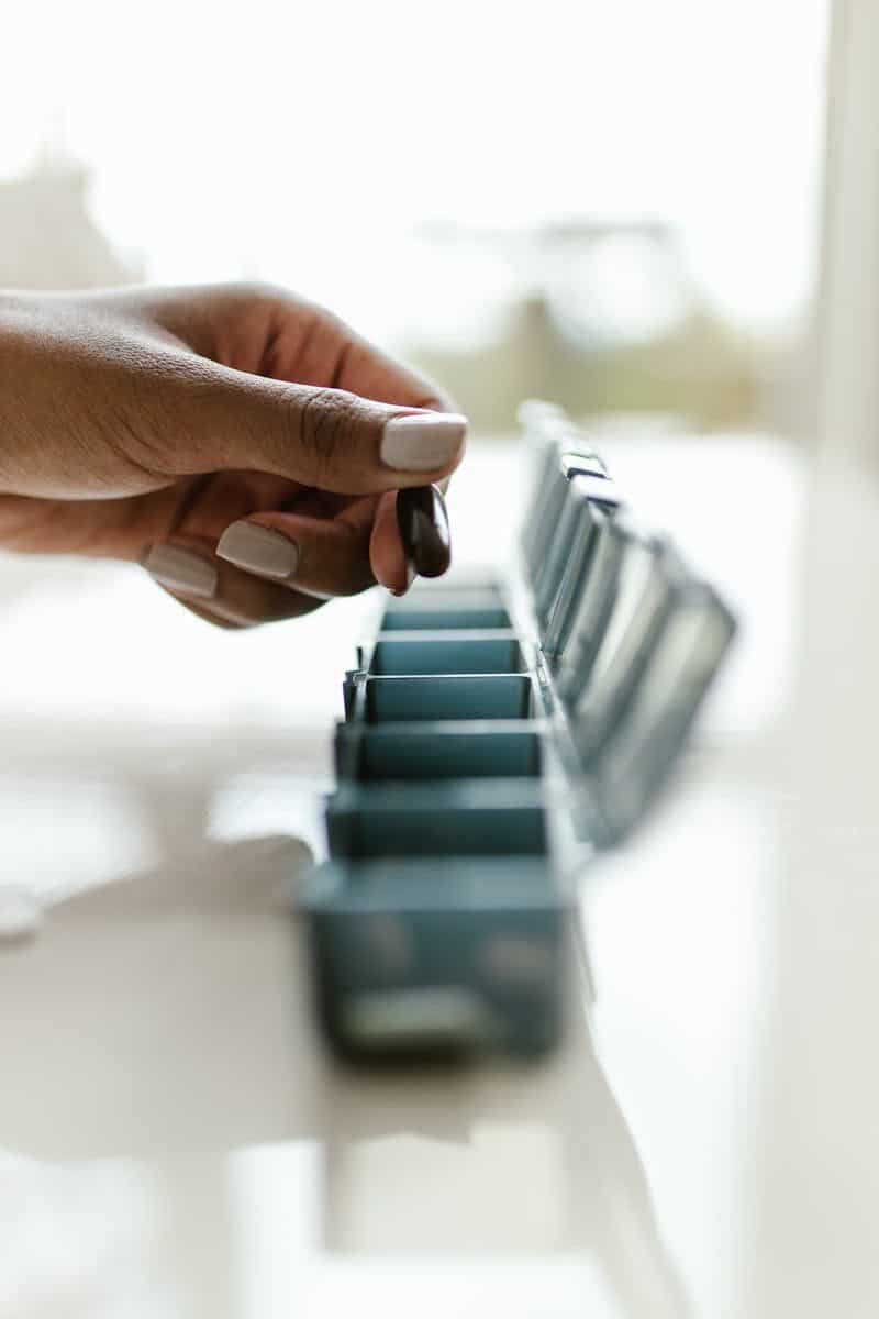 Close-up of a hand holding a pill above a weekly pill organizer, emphasizing medication routine.